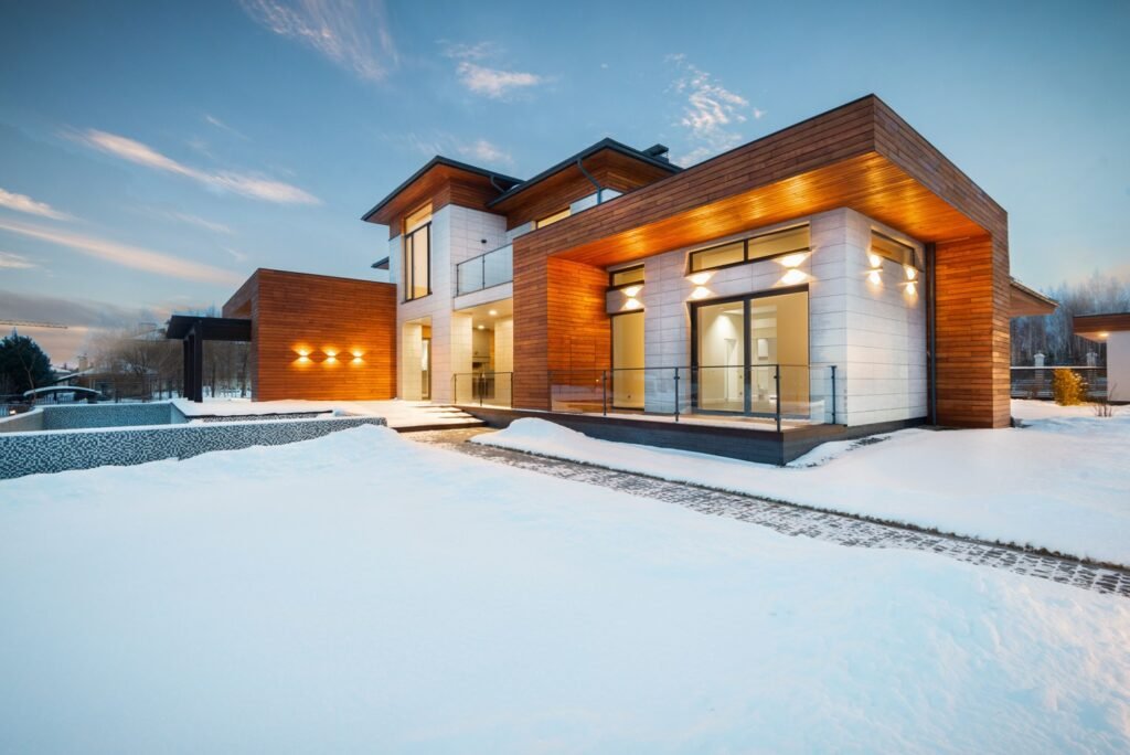 Contemporary home with warm exterior lighting surrounded by winter snow.