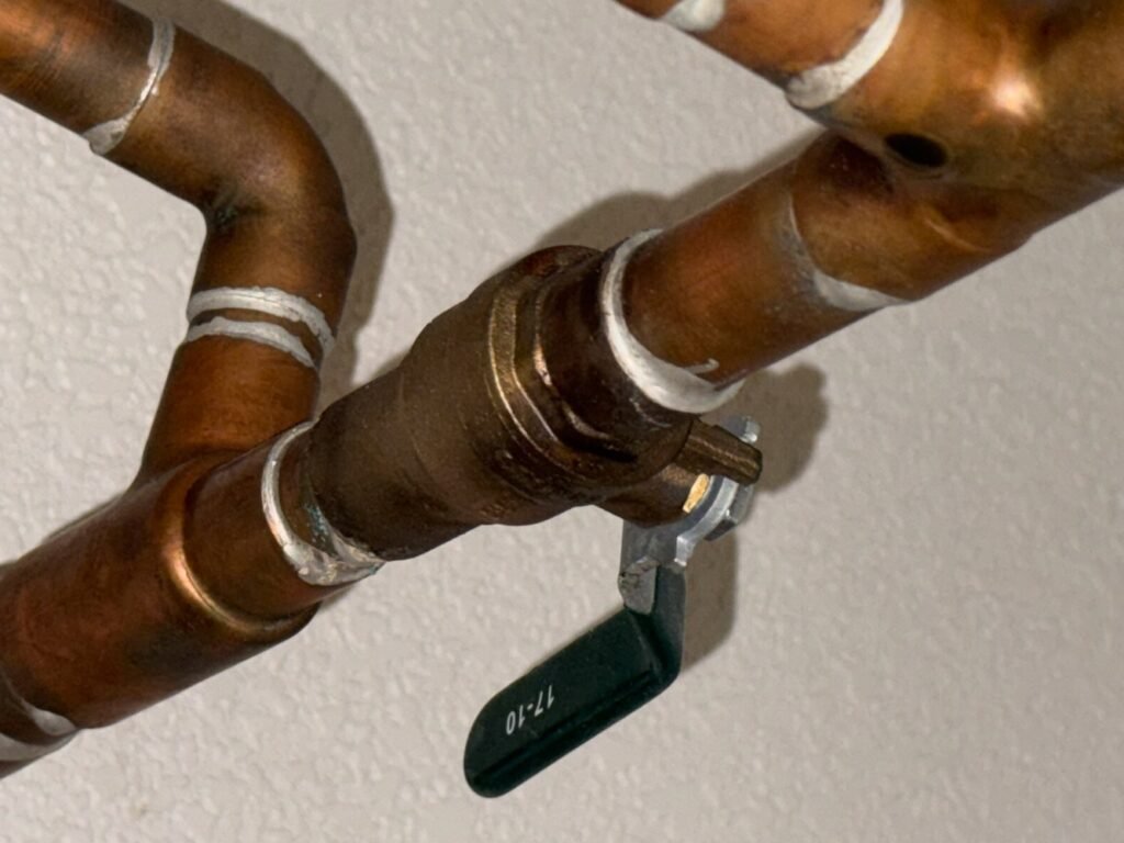 Green-handled water shutoff valve connected to copper pipes.