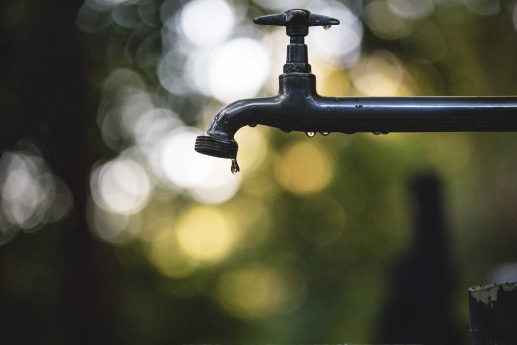 Outdoor metal faucet with water droplets and a softly blurred garden background.
